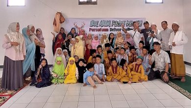 Sekelompok orang, termasuk anak-anak, berpose dalam ruangan dengan spanduk Idul Adha di belakang.